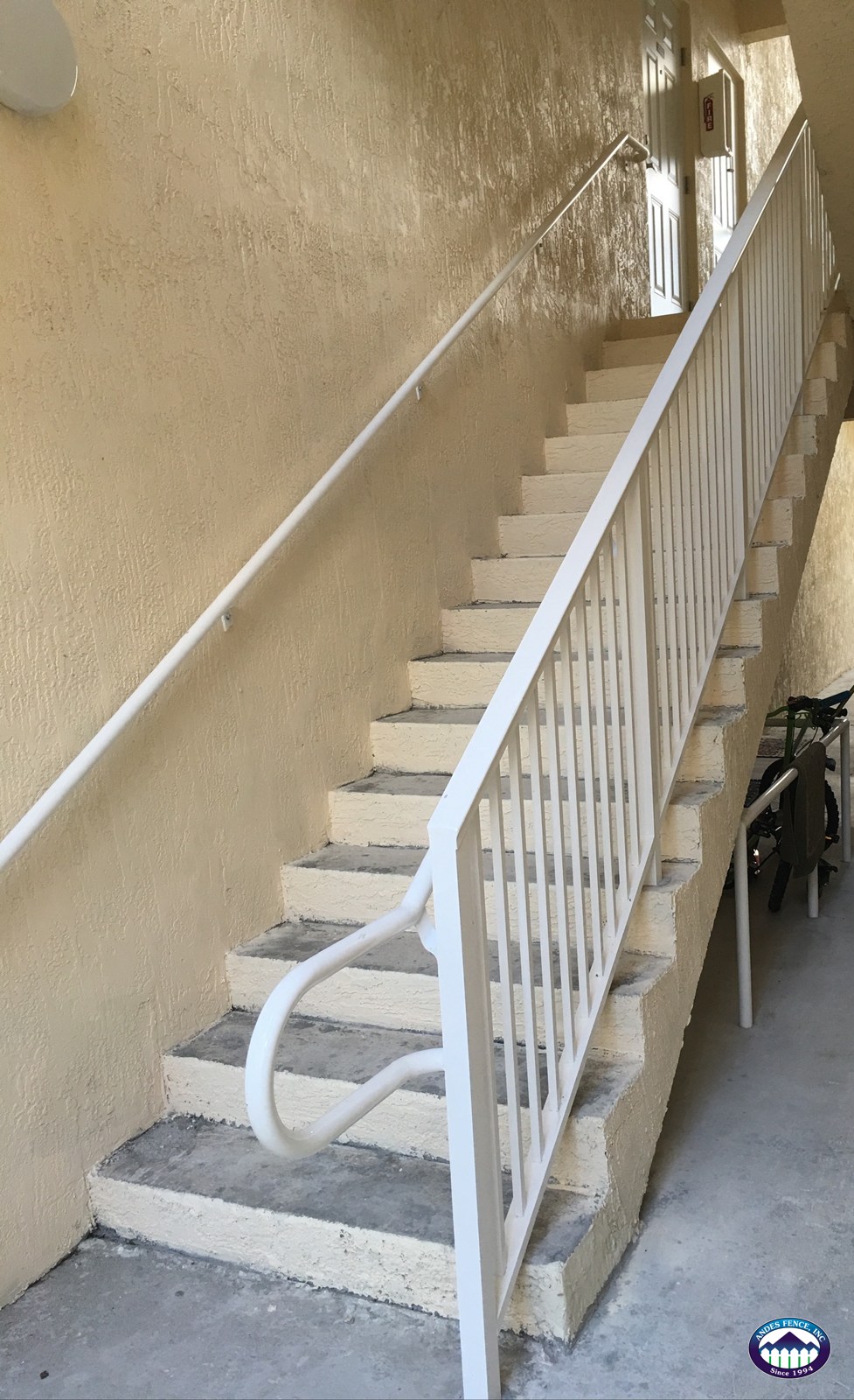White stair railing and wall-mounted handrail along an exterior staircase in an Andes Fence project.
