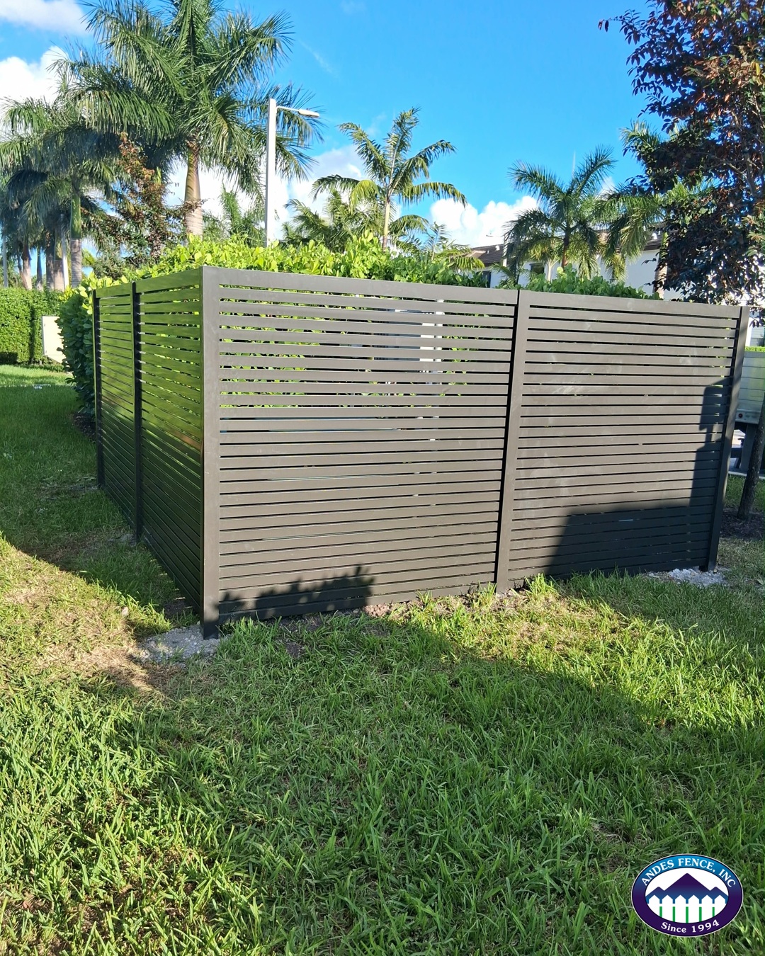 Horizontal slat fence panels meeting at a corner beside landscaping
